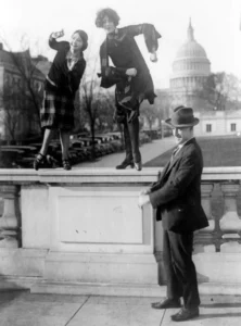 Rep. T.S. McMillan of Charleston, S.C. with flappers, Miss Ruth Bennett and Miss Sylvia Clavins, who are doing the Charleston on railing, with U.S. Capitol in background; Source: Library of Congress, public domain