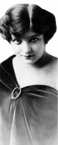 Head-and-shoulders photograph of a young woman with dark bobbed hair in an off-the-shoulder wrap, reproduced in the 1915 newspaper feature as the head of the 1915-model Show Girl.