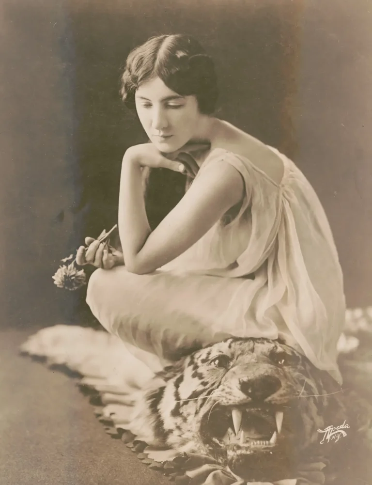 Audrey Munson in a sheer gown, crouched on a tiger-skin rug, in a 1916 Apeda studio portrait made to publicize her film Purity
