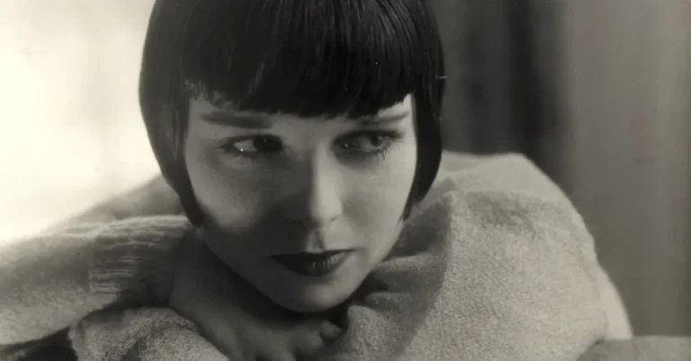 Louise Brooks photographed by Edward Steichen in August 1928, leaning over a chairback in a soft light wrap, wearing the dark bob that became her signature. Cropped from the full frame.