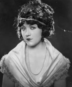 Studio portrait of silent film actress Marie Prevost, about 1923, with dark curled hair and a ribboned headband. Public domain.