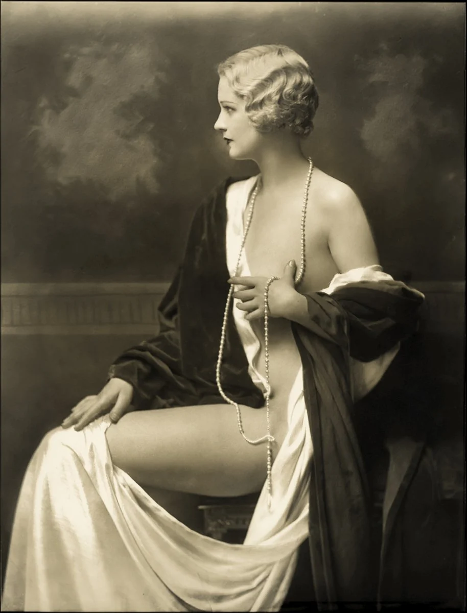 Marie Stevens by Alfred Cheney Johnston, ca. 1930: seated in left profile with a platinum marcel wave, a long strand of pearls and a dark velvet robe slipping from her shoulders over white satin