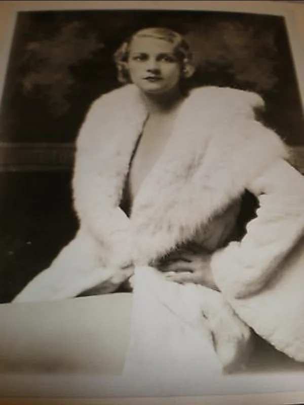 Front of a Culver Pictures file print: Marie Stevens by Alfred Cheney Johnston, seated in a white fur coat before the same painted backdrop and carved dado as the pearls photograph