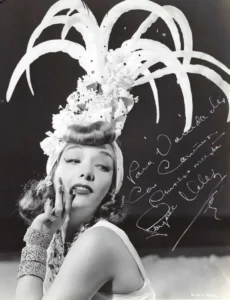 Lupe Velez in a tall feathered headdress, hand at her cheek, on a photograph inscribed and signed in Spanish