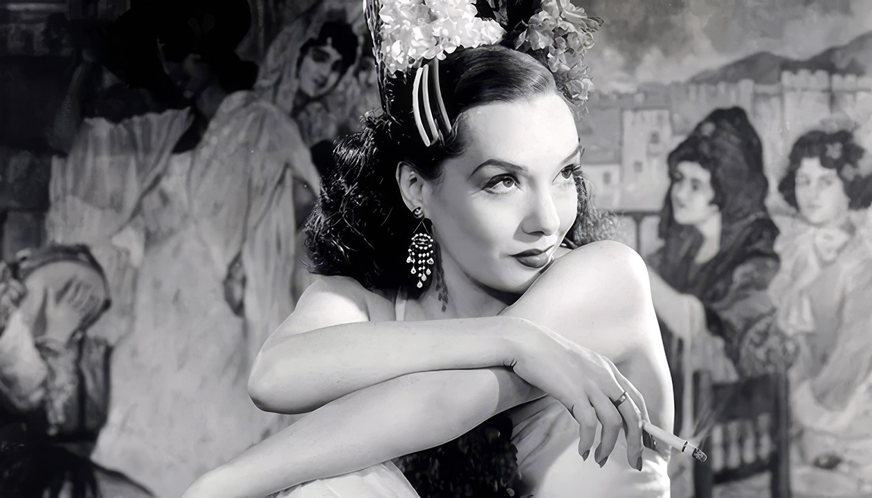 Lupe Velez with flowers and combs in her hair, leaning on folded arms with a cigarette in her hand